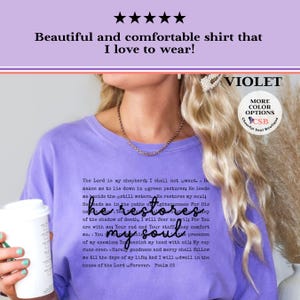 Puede incluir: Una camiseta violeta de cuello redondo con el texto del Salmo 23 impreso en negro. El texto incluye el pasaje completo que comienza con The Lord is my shepherd y termina con Psalm 23, con la frase he restores my soul en una fuente cursiva.