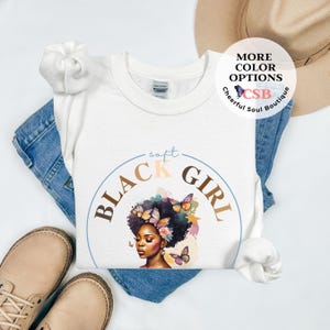 May include: White t-shirt with a graphic of a Black woman with butterflies and flowers. The text "soft black girl" is in a circle around the graphic.
