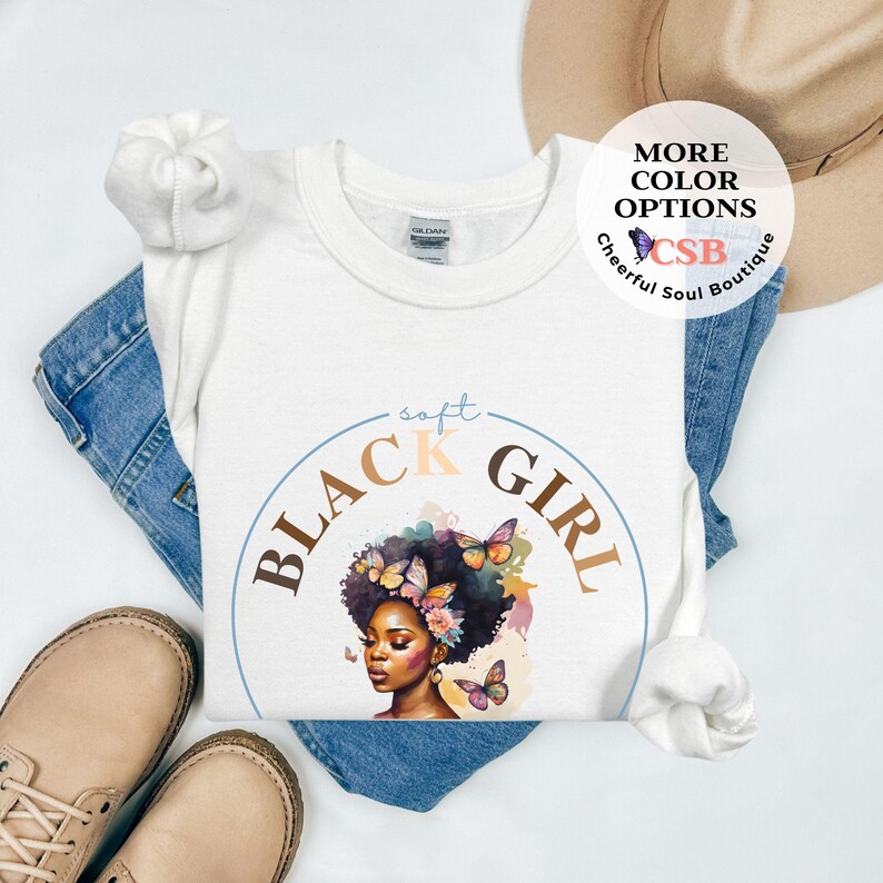 May include: White t-shirt with a graphic of a Black woman with butterflies and flowers. The text "soft black girl" is in a circle around the graphic.
