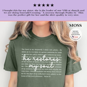 Puede incluir: Una camiseta de manga corta color verde musgo con el texto completo del Salmo 23 impreso en una fuente peque&ntilde;a y clara. La frase he restores my soul est&aacute; impresa en una letra cursiva blanca m&aacute;s grande en el centro del pecho.
