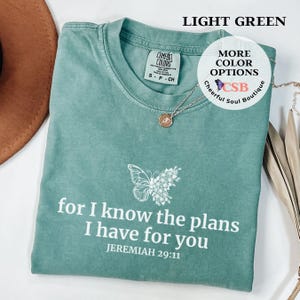 May include: Light green t-shirt with a white butterfly and floral design. The shirt has the text "for I know the plans I have for you JEREMIAH 29:11" printed on it.