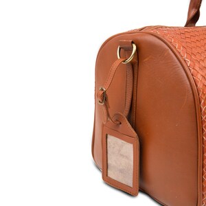 May include: A brown leather travel bag with a woven leather design. The bag has a luggage tag with a blank name card.