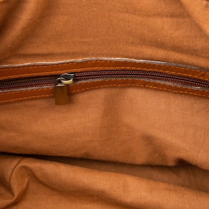May include: The inside of a brown leather bag with a zipper closure. The zipper is open and the lining is a light brown fabric.