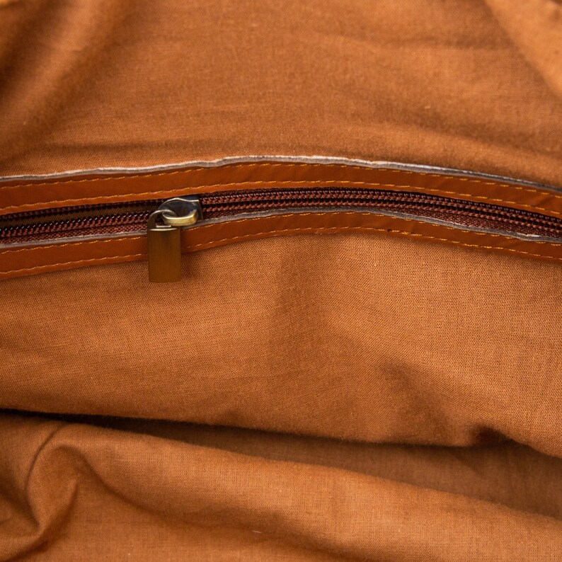 May include: The inside of a brown leather bag with a zipper closure. The zipper is open and the lining is a light brown fabric.