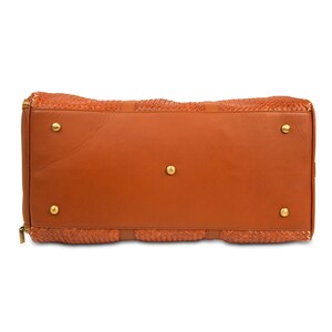 May include: A brown leather duffel bag with a woven pattern and gold accents. The bag has a zipper closure and a flat bottom.
