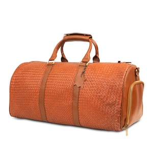 May include: A brown leather duffel bag with a woven pattern and a zippered pocket on the side. The bag has a top handle and a shoulder strap.