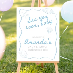 Könnte beinhalten: Ein weißes Schild auf einer Holzstaffelei mit dem Text "Sea you soon, baby" in Hellblau. Das Schild heißt die Gäste zur Babyparty von Amanda willkommen. Dekorative Muscheln und ein Seestern sind ebenfalls abgebildet. Ballons in Pastellfarben sind im Hintergrund.