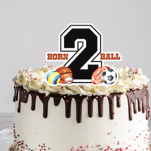 Peut inclure: Un gâteau blanc avec un glaçage au chocolat et des pépites. Le gâteau est décoré d'un topper noir en forme de chiffre "2" avec les mots "BORN" et "BALL" de chaque côté. Le chiffre est entouré d'illustrations aquarelle de différents ballons de sport.