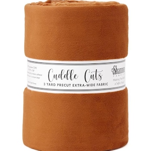 May include: A roll of brown fabric labeled "Cuddle Cuts" with the text "3 Yard Precut Extra-Wide Fabric." The fabric is a solid color and appears soft. The roll is wrapped with a white band.