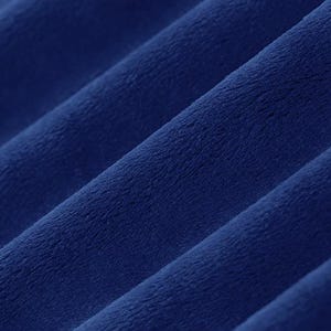 May include: Close-up of a deep blue, plush fabric. The material is soft and velvety, with visible diagonal folds and a slight sheen. The texture suggests a comfortable textile, possibly for clothing or home decor.