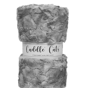 May include: A roll of gray Cuddle Cuts minky fabric, pre-cut to 3 yards. The fabric is soft and plush, with a textured, wavy surface. The product is wrapped with a white label that reads "Cuddle Cuts".