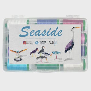 May include: A clear plastic storage case containing 12 large spools of thread. The label features the text Seaside, Barbara Persing, Island Batik, and Aurifil, alongside illustrations of various shorebirds in shades of blue, purple, and orange.