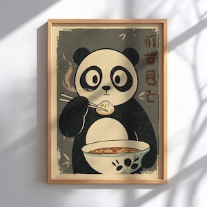 May include: A framed wall art print featuring a black and white panda holding chopsticks and eating a dumpling over a bowl of soup. The background is a muted grey with distressed textures and stylised Asian characters on the right side.