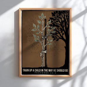 Peut inclure: Une impression d'art encadrée représentant un jeune plant attaché à un tuteur en bois, avec la silhouette d'un grand arbre en arrière-plan. Le texte indique : TRAIN UP A CHILD IN THE WAY HE SHOULD GO PROVERBS 22:6. Palette de brun, noir et vert.