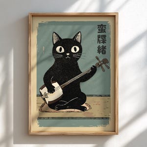May include: A framed art print featuring a black cat playing a shamisen, a traditional Japanese stringed instrument. The cat is depicted with large, expressive eyes and is seated on a cushion. The background is a muted teal with Japanese text.