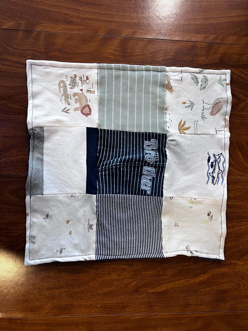 May include: A rectangular patchwork quilt featuring various fabric patterns and colors. The quilt includes animal prints, striped patterns, and the word "Brother" in blue. The quilt is bordered with a white fabric.