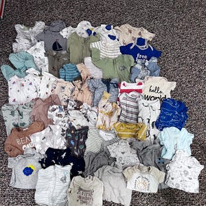 May include: A collection of baby clothes in various colors and styles. The assortment includes onesies, shirts, and zip-up sleepers. Some items feature prints like dinosaurs, sailboats, and the text "hello world".