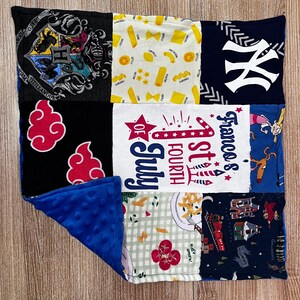 May include: A patchwork blanket featuring various fabric patterns. Designs include a Hogwarts crest, pasta shapes, a New York Yankees logo, red cloud shapes, "1st of July" text, and cartoon characters. The blanket has a blue, textured backing.
