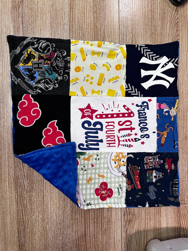 May include: A patchwork blanket featuring various fabric patterns. Designs include a Hogwarts crest, pasta shapes, a New York Yankees logo, red cloud shapes, "1st of July" text, and cartoon characters. The blanket has a blue, textured backing.