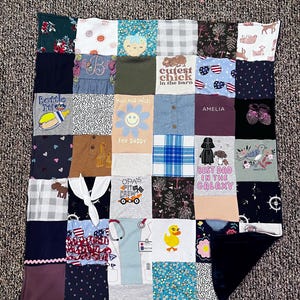 May include: A patchwork quilt made from various fabric squares. The squares feature different patterns, colors, and text, including "Cutest Chick in the Barn," "Hugs and Smiles," and "Best Dad in the Galaxy." The quilt is a mix of textures and designs.