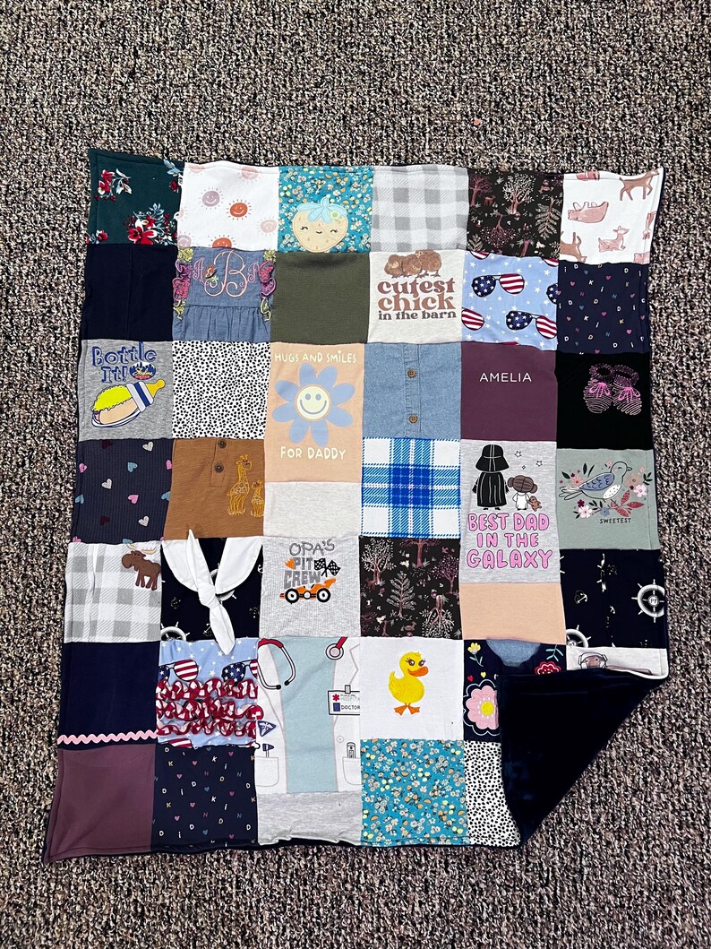 May include: A patchwork quilt made from various fabric squares. The squares feature different patterns, colors, and text, including "Cutest Chick in the Barn," "Hugs and Smiles," and "Best Dad in the Galaxy." The quilt is a mix of textures and designs.