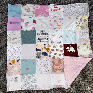 May include: A patchwork baby blanket with various fabric squares in pastel colors. The squares feature prints of animals, strawberries, and the text "lil Nugget" and "SHHH... I'M READING with mommy". The blanket has a pink, textured backing.