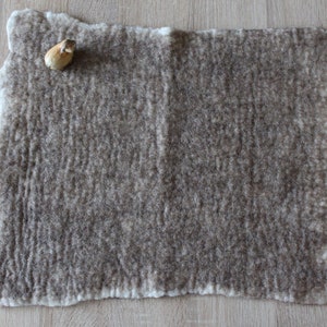 Puede incluir: Una alfombra de fieltro marrón con un borde blanco. La alfombra tiene una superficie texturizada y es rectangular.
