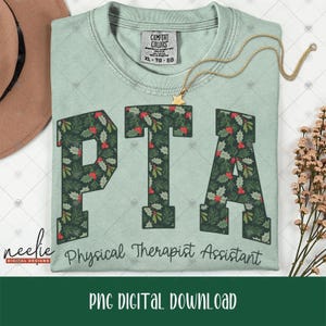 May include: A light green t-shirt featuring the letters PTA in a dark green holly and berry pattern. Below the letters, the text Physical Therapist Assistant is printed in a dark green script font. The shirt has a Comfort Colors brand neck label.