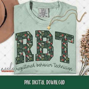May include: A light green crewneck t-shirt featuring the large block letters RBT filled with a pattern of green holly leaves and red berries. Below the letters, the text reads registered behavior technician in a dark cursive script font.