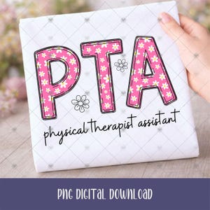 May include: A white t-shirt featuring the letters PTA in a bold, pink font filled with a white daisy pattern. Below the letters, the text physical therapist assistant is written in a black, cursive script. Two small, outlined daisy icons are present.