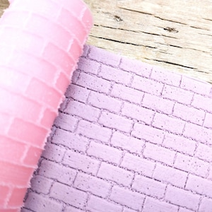 May include: A pink silicone rolling pin with a brick pattern, used for creating textured designs on fondant or clay.