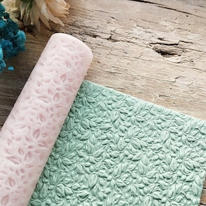 Puede incluir: Un rodillo rosa con un diseño floral y una estera de silicona verde con un diseño floral similar.