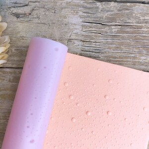 Könnte beinhalten: Nahaufnahme eines rosa und hellrosa strukturierten Papiers mit einem Muster aus kleinen weißen Punkten. Das Papier ist aufgerollt und die Kante ist sichtbar.