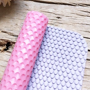 Op de afbeelding: Een roze siliconen deegroller met een textuurpatroon van overlappende cirkels. De deegroller ligt op een paarse siliconenmat met een textuurpatroon van overlappende cirkels.