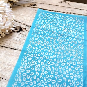 Puede incluir: Una plantilla azul con un diseño de estampado de leopardo blanco. La plantilla está hecha de un material delgado y flexible, ideal para crear un diseño de estampado de leopardo en una variedad de superficies.