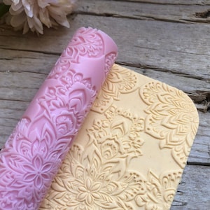 Op de afbeelding: Een roze en beige deegroller met een gedetailleerd bloemenpatroon. De deegroller is gemaakt van siliconen en is ontworpen om decoratieve patronen op fondant of deeg te creëren.