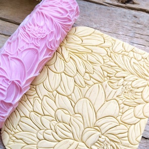 Könnte beinhalten: Eine rosa Rolle mit einem Blumenmuster wird über eine Platte gelben Fondants mit einem passenden Blumenmuster gerollt.