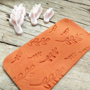 May include: A set of four leaf-shaped cookie cutters and a rolling pin with a leaf pattern. The cookie cutters are pink and the rolling pin is orange.