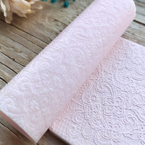 May include: A pink silicone rolling pin with a lace pattern embossed on the surface. The rolling pin is rolled out on a flat surface, revealing the lace pattern.