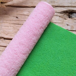 Op de afbeelding: Een opgerolde roze en groene pluche stof. De stof is zacht en pluche.