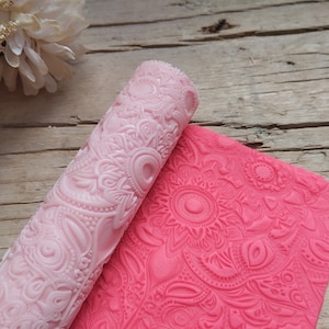 Könnte beinhalten: Eine rosa und rote Silikon-Nudelholz und eine passende Silikonmatte mit einem Blumenmuster. Das Nudelholz ist auf der Matte aufgerollt.