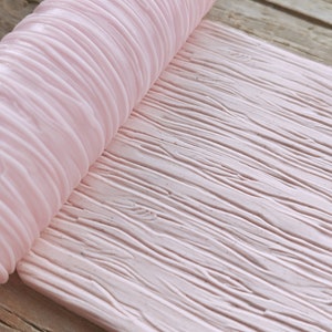 May include: A light pink, textured rolling pin with a wood grain pattern. The rolling pin is partially rolled out, revealing the detailed wood grain texture. The background is a wooden surface.