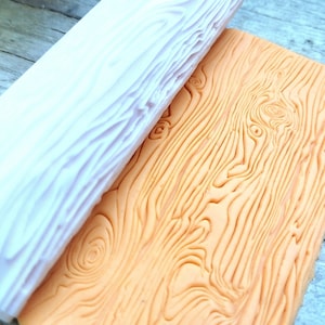 Puede incluir: Un rodillo de silicona blanco con un patrón de veta de madera en la superficie. El rodillo se está utilizando para extender una lámina de fondant naranja con un patrón de veta de madera.