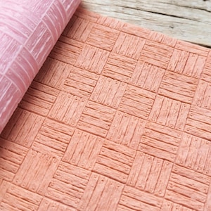 Puede incluir: Una lámina de silicona rosa con un patrón de tablones de madera en relieve. La lámina de silicona está enrollada y el patrón de tablones de madera es visible.
