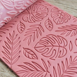Può includere: Mattarello rosa con un design a foglie tropicali. Il mattarello viene utilizzato per creare motivi in rilievo su fondant o pasta.