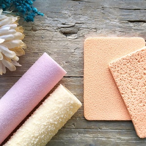 Può includere: Due spugne per il trucco testurizzate, una rosa e una beige, con una superficie testurizzata. Le spugne sono su una superficie di legno.