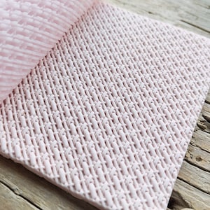 Puede incluir: Una estera de hornear de silicona rosa con un patrón tejido. La estera es flexible y se puede usar para una variedad de proyectos de horneado.