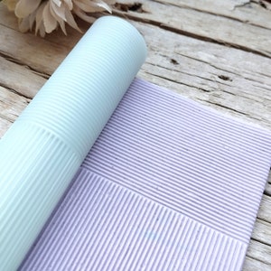 May include: A roll of light blue textured paper with a light purple textured paper underneath. The paper has a ribbed pattern.