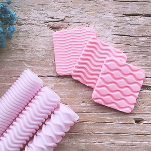 Pode incluir: Três rolinhos de cabelo cor-de-rosa com textura ondulada. Os rolinhos são feitos de um material macio e flexível e são projetados para criar ondas ou cachos soltos no cabelo.