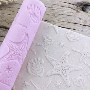 Può includere: Un mattarello rosa con un designo in rilievo di stelle marine e conchiglie. Il mattarello viene utilizzato per creare un'impronta del design su fondant o pasta.